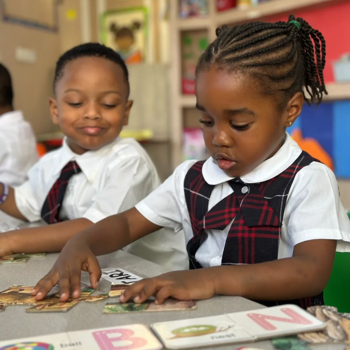 Two early-years students completing an alphabet puzzle together at a classroom table