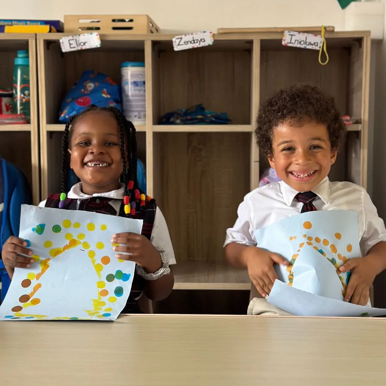 Two elementary students smiling and holding up their dot paintings