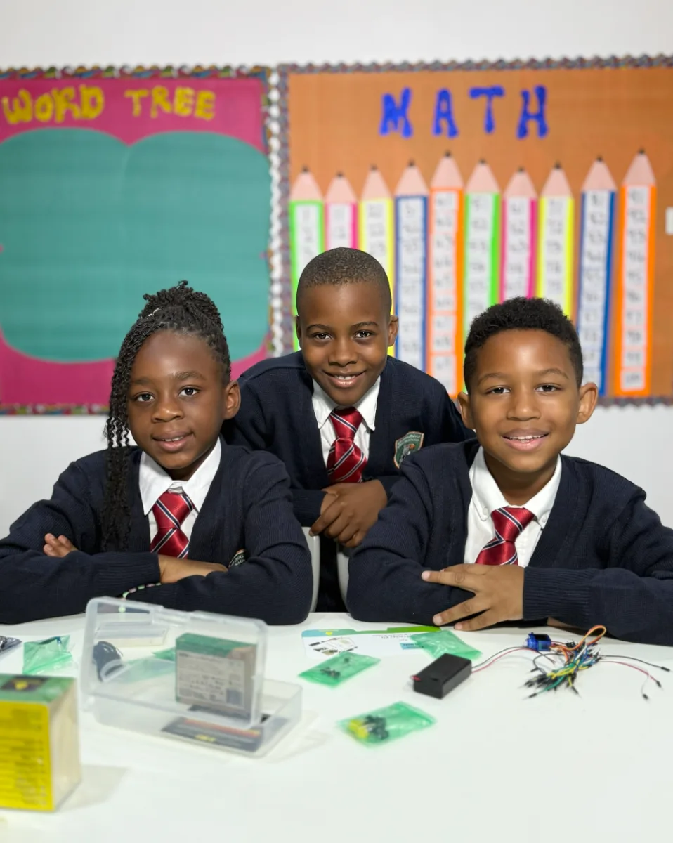 Three students seated together with an electronics project kit in a classroom